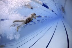 Ein Schwimmer von unter Wasser aufgenommen wirbelt mit den Beinen Luftbläschen auf
