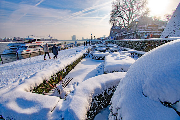 Spaziergänger am schneebedeckten Rheinufer Richtung UN Campus