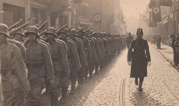 Marschierende Wehrmachttruppe in einer Bonner Straße mit geflaggten Hakenkreuzfahnen (1939)
