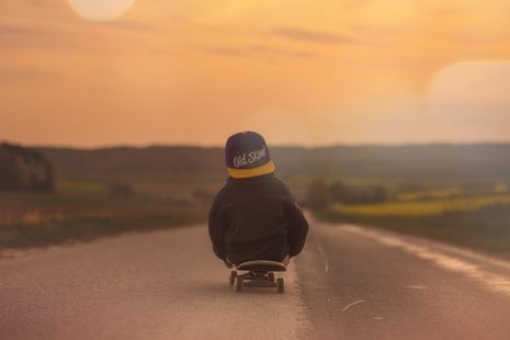 Junge sitzt auf Skateboard und rollt eine Straße runter