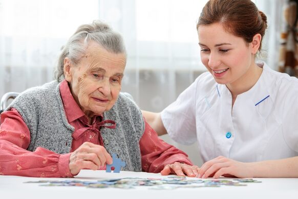 Seniorin mit Pflegern bei einem Puzzlespiel