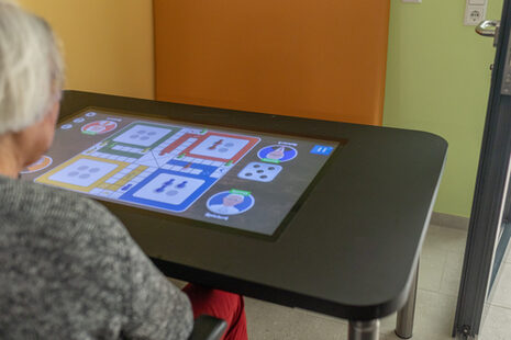 Eine Seniorin sitzt vor einem digitalen Spieltisch mit Spielkartensymbolen