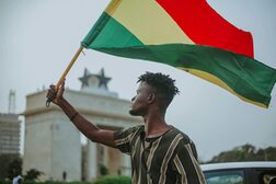 Ein dunkelhäutiger Mann hält eine Fahne Ghanas in die Höhe