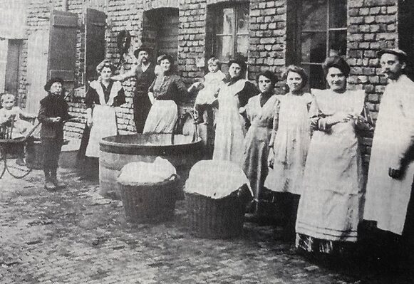 Das historische Foto aus dem Jahr 1900 zeigt Frauen vor einem großen Waschbottich und kleineren Körben voller Wäsche