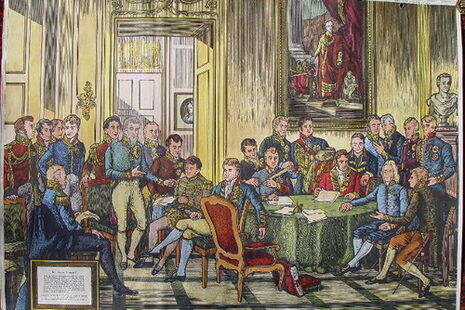Zu sehen ist ein buntes Bild mit vielen Menschen in einem Saal. Sie stehen und sitzen um einen runden Tisch. Es handelt sich um Bild des Wiener Kongresses.