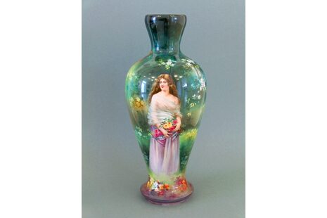 Zu sehen ist eine grüne, leicht transparent wirkende Vase, die eine Frau mit bunten Blumen in der Hand zeigt.