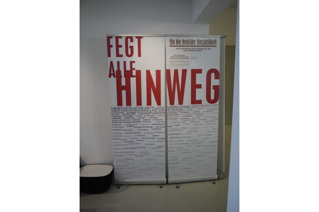 Das Foto zeigt eine Stellwand, auf der in großen roten Buchstaben „Fegt alle hinweg“ steht. Darunter sind kleinere Schriftzüge.