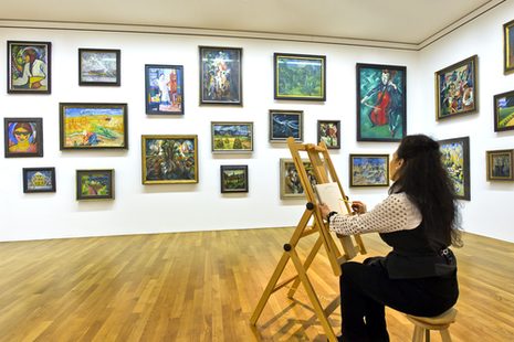 Eine Frau sitzt in einem Ausstellungssaal des Kunstmuseums Bonn an einer Staffelei und malt