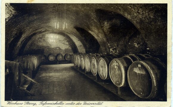 Zu sehen ist ein Schwarz-Weiß-Bild. Es zeigt einen Keller mit Weinfässern. Es handelt sich um den Weinkeller unter der Universität des Weinhauses Streng.