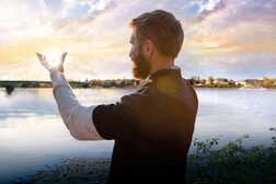 Ein Mann steht am Rheinufer und hält die Hand so, als ob der die untergehende Sonne in Händen hielte