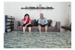 Ein Mann und eine Frau sitzen auf einer Couch im Wohnzimmer, der Fußboden ist von Wasser überflutet.