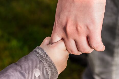 Eine Kinderhand umfasst den Zeigefinger eines Erwachsenen