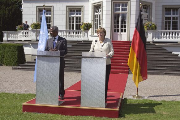 Bundeskanzlerin Angela Merkel und UNO-Generalsekretär Kofi Annan an Rednerpulten in einem Park