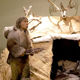 Figur eines in Fell gekleideten Neandertalers vor seiner Hütte