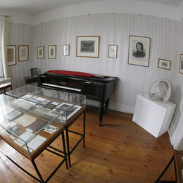 Vitrine mit Dokumenten, ein historisches Klavier und Gemälde im Gedenkzimmer des Schumannhauses
