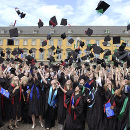 Absolventen im Talar werfen vor dem Unihauptgebäude ihre Hüte in die Luft