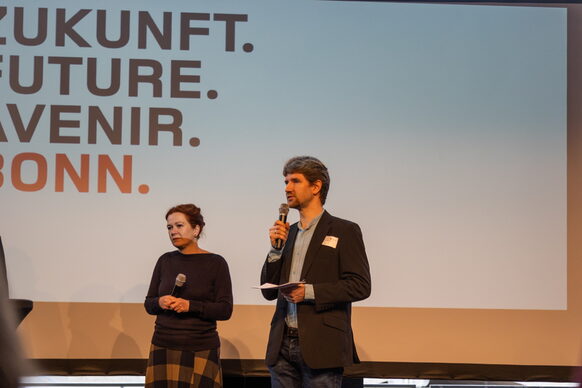 Oberbürgermeisterin Katja Dörner und ein Moderator sprechen auf einer Bühne.