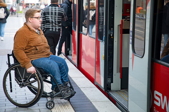 Ein Mann sitzt im Rollstuhl und wartet an einer barrierefreien Haltestelle auf eine Straßenbahn.