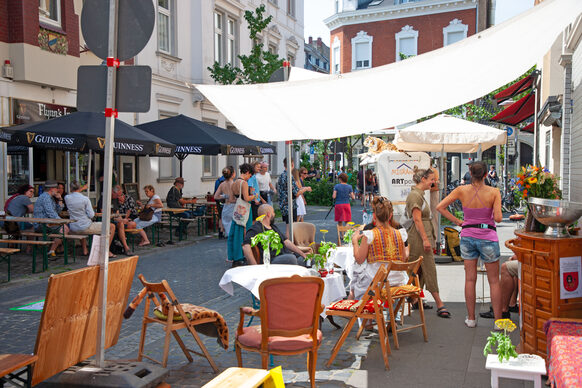 Das Bild zeigt Stühle, Tische und ein Sofa, die in der Altstadt dort stehen, wo sonst Autos parken.