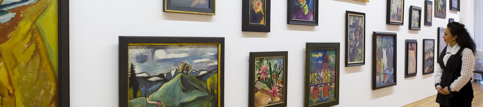 Verschiedene Ölgemälde an einer Wand im Kunstmuseum. Vor der Wand steht eine Frau, die die Bilder betrachtet.