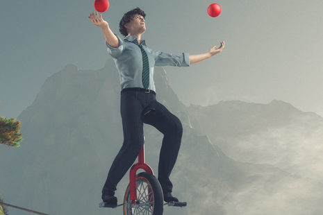 Mann jongliert mit zwei roten Bällen auf Einrad