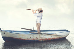 Mann mit Fernrohr steht auf Ruderboot
