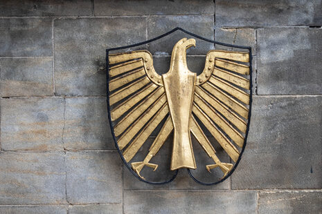Der Bundesadler aus goldfarbigem Metall an einer Mauer