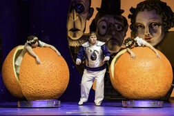 Zwei Frauen stehen in überdimensionierten Orangen, in der Mitte steht ein Mann