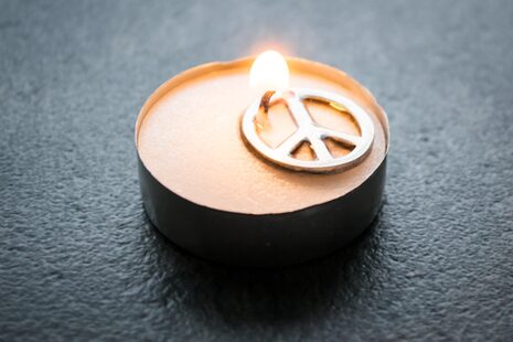 Auf einem angezündeten Teelicht liegt auf Metall das Peace-Zeichen als Bitte um Frieden