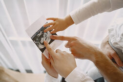Erwachsene und eine Kinderhand zeigen auf ein Ultraschallbild eines Embryos