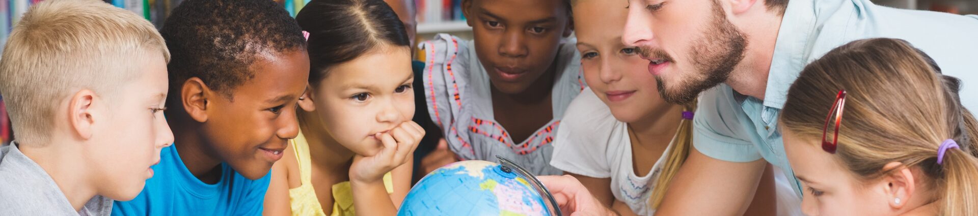 Eine Gruppe von Schülerinnen und Schülern unterschiedlicher Herkunft beugt sich über einen Globus