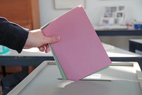 Eine Hand wirft farbige Stimmzettel in eine Wahlurne