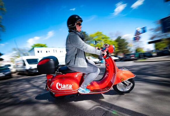 Das Foto zeigt eine Frau, die auf einem roten E-Roller fährt.