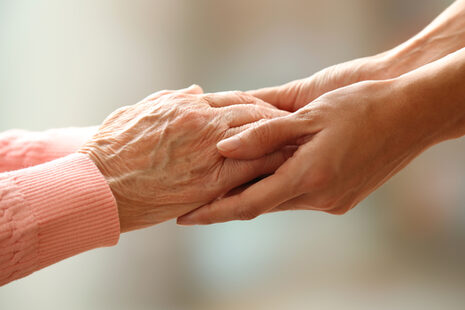 Eine junge Person reicht einer Seniorin beide Hände