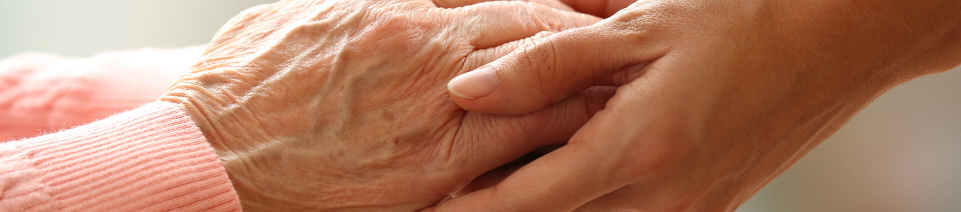 Eine junge Person reicht einer Seniorin beide Hände