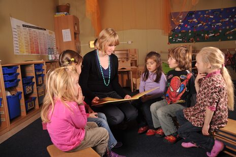 Eine Frau liest Mädchen im Kindergarten aus einem Buch vor