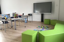 Schulungsraum mit Großbildfernseher, Lehrmaterial und grüner Sitzbank