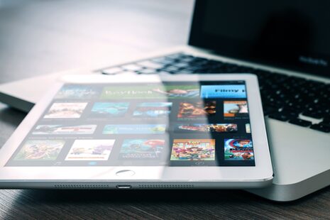 Ein iPad liegt auf einem Macbook. Auf dem iPad zu sehen ist das Angebot einer Streaming-Plattform.