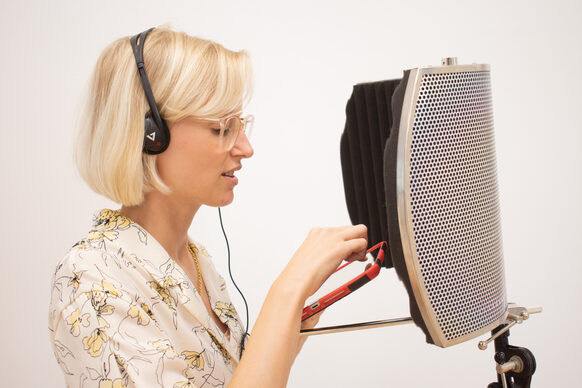 Eine Frau spricht bei einer Audioaufnahme in ein Mikrofon hinein