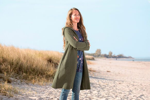 Junge Frau mit grüner Langjacke am Strand vor Dünen