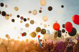 Rote, schwarze und weiße Luftballons schweben über einem Publikum, das die Hände in die Luft reckt