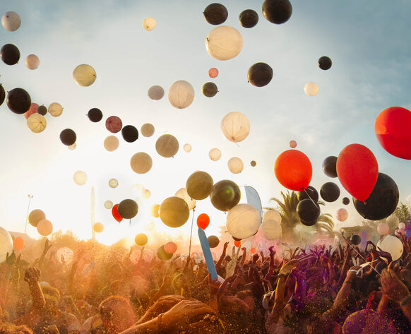 Rote, schwarze und weiße Luftballons schweben über einem Publikum, das die Hände in die Luft reckt