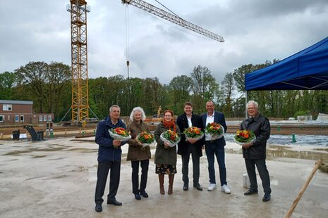 Das Foto zeigt sechs Personen mit Blumen in der Hand auf der Bodenplatte des Neubaus von Haus Elisabeth.