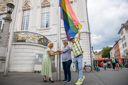 Bürgermeisterin Melanie Grabowy und Vertreter des Vereins R(h)einqueer hissen die Regenbogenfahne am Alten Rathaus.