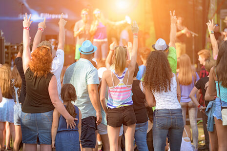 Menschen verschiedenen Alters stehen beim einem Konzert vor einer Bühne und jubeln