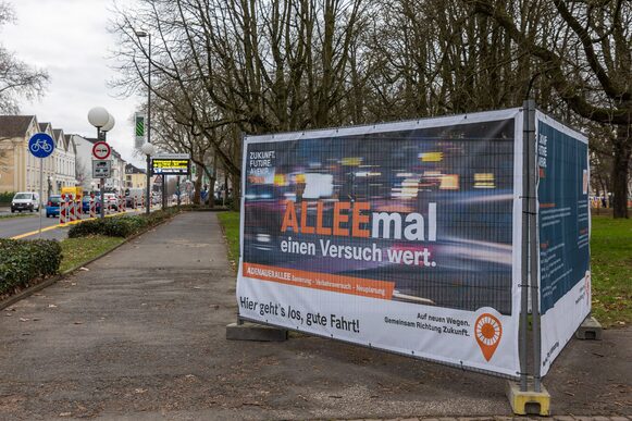 Ein großformatiges Plakat mit der Aufschrift "ALLEEmal einen Versuch wert" macht an der B9 auf den Verkehrsversuch auf der Adenauerallee aufmerksam.