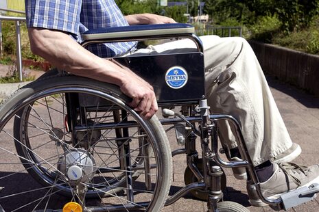 Detailaufnahme der Beine und Arme eines im Rollstuhl sitzenden Mannes