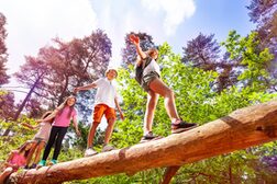 Eine Gruppe Jugendliche balanciert über einen abgestorbenen Baumstamm