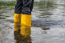 Eine Person mit gelben Gummistiefeln steht im steigenden Hochwasser