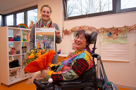 Das Bild zeigt Tanja Rösgen, die von Sozialdezernentin Carolin Krause einen Blumenstrauß und ein Foto ihres Motivs in der Engagement-Galerie zum Dank überreicht bekommt.